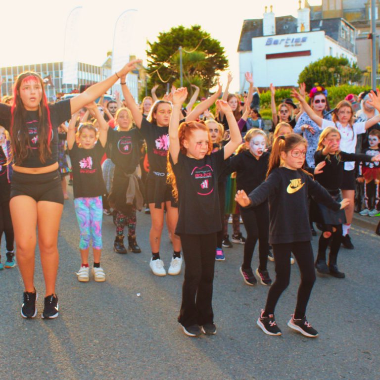 A group raises their arms during a street dance. Newquay Zombie Crawl 2024.