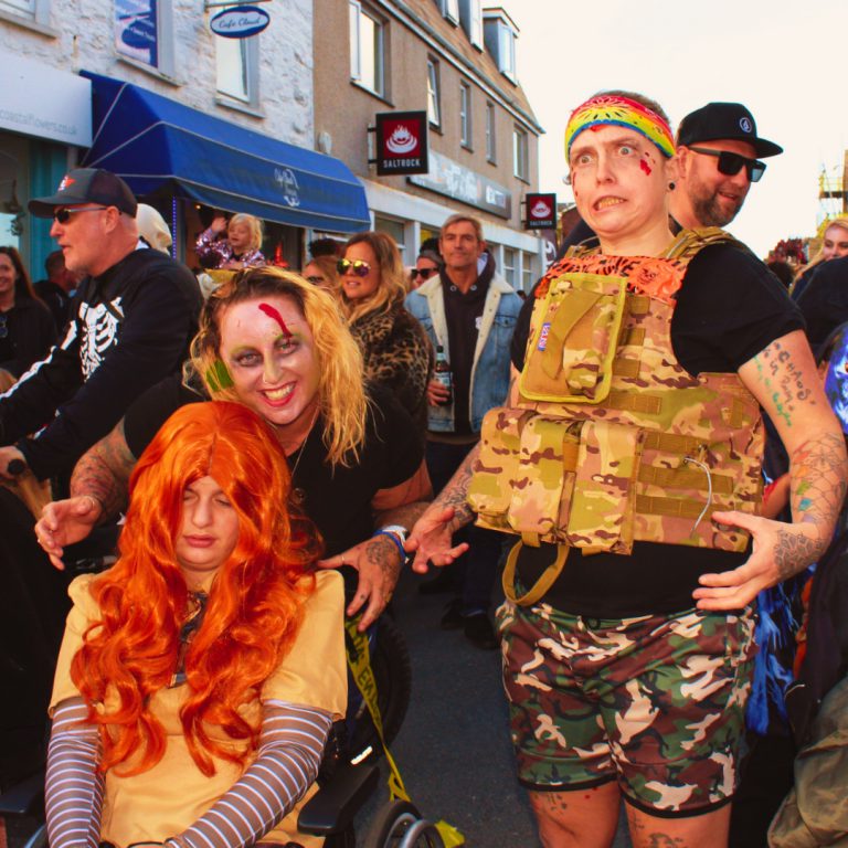 Costumed participants pose, including someone wearing camouflage and a colourful headband. Newquay Zombie Crawl 2024.